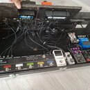 Černý dřevěný pedálboard s několika efekty a napájecím zdrojem. V horní části je připevněn zdroj s nápisy "Celine" a "JOYO POWER SUPPLY". V dolní čás…