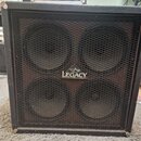 Černý kytarový reproduktorový box s kovovou mřížkou a čtyřmi membránami. Uprostřed mřížky je umístěno bílé logo s nápisem LEGACY a trojúhelníkovým sy…