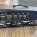 Černý kytarový kombo zesilovač s rukojetí nahoře. Na zadním panelu je vidět nápis LINE 6 Explorer a technické specifikace. Horní část zadní strany tv…