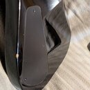 Detailní pohled na černý, vysoce lesklý povrch hudebního nástroje. Na ploše je vidět malá odщеpka nebo skvrna světle hnědé barvy. Na povrchu nejsou ž…