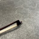 Detailní záběr na hrot smyčce z tmavého dřeva s bílým vlasem. Koncová část hůlky je zaoblená a vykazuje mírné opotřebení povrchu v místě zakončení. N…