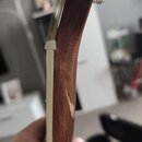 Detailní pohled na hmatník a bočnici krku kytary z tmavého dřeva s bílým lemováním. Na dřevěném povrchu bočnice jsou viditelné škrábance a odřeniny l…