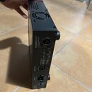 Černý kovový zesilovač s ventilátorem na horní straně. Na zadním panelu jsou nápisy BALANCED OUTPUT, PHON DIRECT OUT, POST EQ a SPEAKER OUT. Jsou zde…
