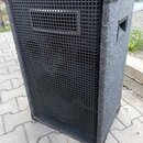Šedý reproduktor v bedně potažené texturovaným materiálem. Přední stranu tvoří černá kovová mřížka s obdélníkovým výřezem v horní části. Rohy jsou ch…