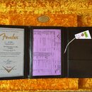 Fotografie zachycuje otevřený hnědý kožený dokument s certifikátem pravosti a specifikací nástroje, umístěný v pouzdře s žlutým plyšovým výstýlkou. N…