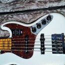 Bílá elektrická basová kytara s hnědo-červeným želvovinovým pickguardem v polstrovaném kufru. Na pickguardu je vidět logo Fender a nápis ULTRA. Ovlád…