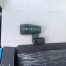 Černý kondenzátorový mikrofon s nápisem e604 a logem SENNHEISER. Nástroj je umístěn v bílém kartonu vedle černé krabičky a plastového sáčku. Povrch m…