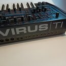 Stříbrný syntetizátor s klávesnicí a tmavě hnědými dřevěnými bočními panely. Na přední hraně je velký nápis VIRUS TI a řada konektorů s popisky jako…