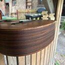 Detailní pohled na korpus akustické kytary z boku. Kytara má hnědý povrch s výraznou tmavou sletovanou strukturou dřeva na bocích. Na horní hraně kor…