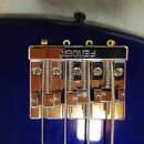 Detail chromovaného mostu na modrém trupu basové kytary. Na horní části je vyryt nápis FENDER. Most obsahuje čtyři saddles s viditelnými pružinami a…