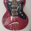 Vínová polodublová elektrická kytara s černým pickguardem a třemi humbuckery. Na těle je pod mostem viditelný nápis Ibanez. Nástroj má chromovaný mos…