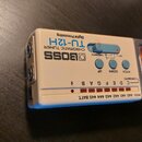 Bílý digitální chromatický tuner značky BOSS, model TU-12H. Na zařízení je nápis CHROMATIC TUNER a Digital Processing. Přístroj obsahuje modré ovláda…