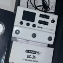 Bílý efektový pedál s nápisem LINE 6 HX STOMP. Zařízení má displej, čtyři ovládací tlačítka a otočný potenciometr VOLUME. Pod pedálem je umístěna bíl…