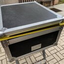 Černý transportní kufřík s hliníkovými hranami a kovovými rohy. Povrch víka vykazuje množství drobných škrábanců a oděření. Na přední straně je umíst…