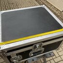 Černý transportní kufr s hliníkovými hranami a kovovými rohy. Na horní straně je položen žlutýv metr, který ukazuje délku přibližně 66 cm. Kufr má dv…