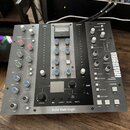 Šedý studiový procesor s nápisem Solid State Logic na spodní liště. Zařízení obsahuje řadu knoflíků, přepínačů a jeden analogový VU metr. V pravé čás…