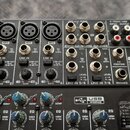 Šedý mixážní pult značky behringer s nápisem H204USB. Horní panel obsahuje vstupy MIC, LINE IN a STEREO AUX RETURNS s různými typy konektorů. V pravé…