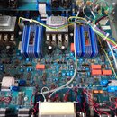 Fotografie zachycuje vnitřek elektronického zařízení s modrou základní deskou a četnými komponenty. Jsou zde dva stříbrné transformátory s nápisy jen…