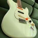 Bílá elektrická kytara typu Stratocaster s bílým pickguardem a hnedým hmatníkem. Nástroj má tři snímače, tři ovládací knoflíky v krémové barvě a jede…