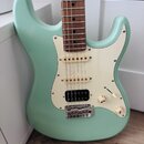 Světle zelená elektrická kytara s bílým pickguardem a hnedým hmatníkem. Nástroj má konfiguraci snímačů dvou singlů a jednoho humbuckeru, na kterém je…