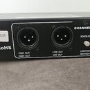 Záběr na zadní část černého elektronického zařízení s kovovým povrchem. Jsou vidět tři konektory XLR a přepínač u nápisů CHANNEL TWO, XOVER FREQ., X1…