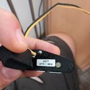 Detailní záběr na černý plastový komponent s připojenými žlutými vodiči. Na bílém štítku je uveden nápis INC77 APTR-1 0830 a nad ním je vyraženo SD 2…