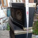 Černý reproduktorový box s kovovými hranami a vrchy v zlatavé barvě. Přední strana je kryta černou kovovou mřížkou, za kterou je viditelný reprodukto…