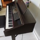 Digitální piano v tmavě hnědém dřevěném korpusu s bílými a černými klávesami. Horní ovládací panel obsahuje množství tlačítek, posuvníků a displej, a…