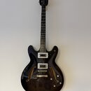Černá polodupatá elektrická kytara s lesklým povrchem a dvěma f-otvory. Na hlavě je bílý nápis Epiphone a na hmatníku viditelné pražce. Nástroj má dv…