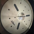 Kruhová mosazná činely s matným povrchem a vyfrézovanými oválnými a kulatými otvory. Na povrchu je černý nápis Zildjian. U středu se nachází bílá pap…