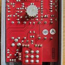 Interiér kovového šasi s červenou plošnou deskou, na které jsou připájené elektronické součástky. Na desce jsou dva bílé plastové potenciometry a náp…