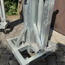 Detailní pohled na spodní část stříbrného kovového stojanu z pozinkovaného profilu. Konstrukce tvoří čtvercová základna s vyztužujícími vzpěrami. Pov…