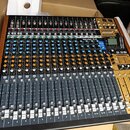 Míčovací pult s černým povrchem a dřevěnými bočními panely. Na přístroji je nápis Model 24 a logo TASCAM u digitálního displeje. Ovládací panel obsah…