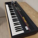 Černý digitální sampler s klaviaturou umístěný na světlém dřevěném stole. Na horním panelu je žlutý nápis Mirage-DSK a pod ním menší text DIGITAL SAM…