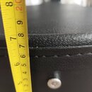 Detailní záběr na černý povrch z texturované syntetické kůže se švem. Vedle povrchu je přiložen žlutýv metr, který ukazuje hodnoty v centimetrech a p…