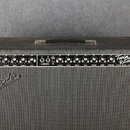 Kytarový kombozesilovač v černém potahu s textilní maskou. Na ovládacím panelu jsou nápisy NORMAL, VIBRATO a Twin Reverb-Amp, dále značka FENDER MUSI…