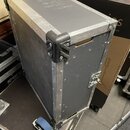 Černý transportní flightcase s hliníkovými hranami a plastovými rohovými chrániči. Bedna je vybavena jedním viditelným zámkem a modrým kolečkem u spo…