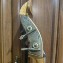 Detail hlavy smyčcového nástroje zCvětlého dřeva s kovovými ladičkami. Na kovové části jsou vidět oxidace, skvrny a patina. Ladičky mají ozubený mech…
