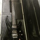 Černá elektrická kytara v tvrdém kufru. Na hlavě hmatníku je bílý nápis HAMER. Kytara má dva humbuckery, jeden ovládací knoflík hlasitosti a jeden tó…