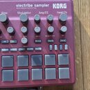 Bordeaux červený sampler s nápisy electribe sampler, KORG a MUSIC PRODUCTION STATION. Zařízení obsahuje několik šerad ovládacích knoflíků pod popisky…