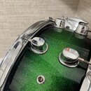 Detailní pohled na horní část bubnu s nasyceně zeleným metalizovaným povrchem typu sparkle. Jsou vidět chromované obruče, dva ladicí šrouby a kovový…