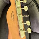 Zadní strana hlavy kytary z přírodního dřeva s chromovanými ladicími kolíky. Na dřevě je černý nápis SERIAL NUMBER MX24048748 a MADE IN ENSENADA. Pov…