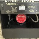 Zadní strana černého kytarového komba s nápisy Quilter™, AVIATOR a CUB. Uprostřed je viditelný reproduktor s červeným štítkem, na kterém je text Quil…
