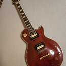 Elektrická kytara typu Les Paul s tmavě červeným prožilkovaným povrchem těla a krčkem s hmatníkem z tmavého dřeva a trapezoidními vložkami. Nástroj m…