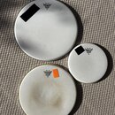 Tři bílé bubnové membrány různých velikostí položené na koberci. Každá z nich nese logo REMO s nápisy Ambassador Coated a Made in USA. Největší membr…