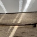 Na dřevěném povrchu leží smyčec s hnědým dřevěným stupněm a bílými vlasmi. V pravé části je černý plastový nebo ebonitový šroubovací mechanismus. Pov…