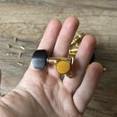 Na dlani je položen ladicí kolík v zlatém provedení s černým plastovým knoflíkem. Na boční části mechanismu je vyryt nápis GOTOH a pod ním malý symbo…