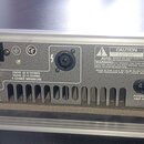 Zadní strana stříbrného zesilovače v kovovém šasi. Na přístroji jsou nápisy „CE“, „200W @ 8 OHMS“, „350W @ 4 OHMS“ a „4 OHMS MINIMUM“. Štítek obsahuj…