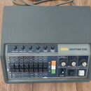 Šedý rytmus stroj s nápisem KORG RHYTHM 55B. Zařízení má ovládací panel s posuvníky pro Bass Drum, Snare Drum, Cymbal, Hi-Hat a TomTom Conga, řadu tl…