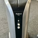 Stříbrný osobní monitor s černým předním panelem a mřížkou reproduktoru v horní části. Na panelu je bílý nápis Roland a pod ním označení PM-03. Jsou…
